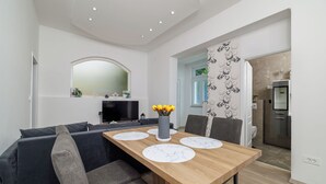 A modern dining area with a wooden table, grey upholstered chairs, and a grey sofa. - Apartment Filip 2 (Crikvenica)