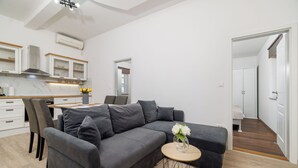 A modern living room with a grey sectional sofa, a round coffee table, and a dining area with a wooden table and chairs. - Apartment Filip 2 (Crikvenica)