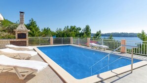 Una piscina con sillones de descanso, una chimenea de piedra y vistas a un lago.