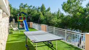 Un balcón con mesa de ping pong, una estructura de juegos infantiles y vista al mar.