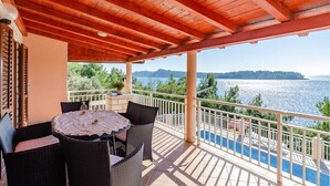 Un espacio al aire libre techado con mesa y sillas, una piscina y vistas al mar y las montañas.