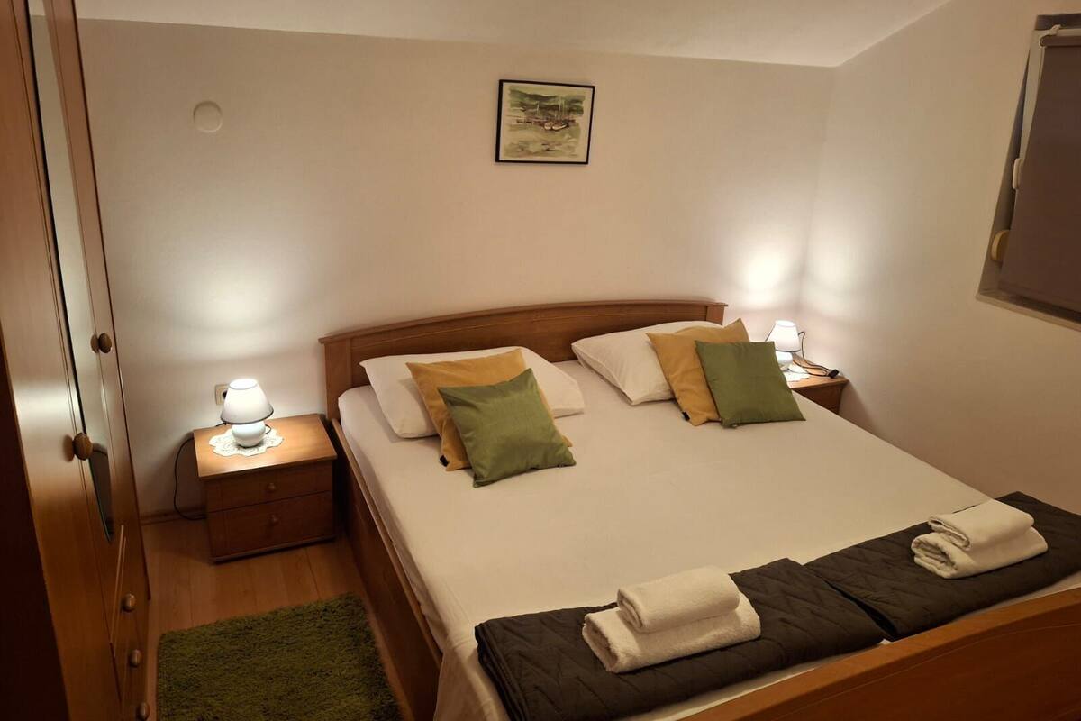 Ein ordentlich eingerichtetes Schlafzimmer mit einem Bett, zwei Nachttischen, einem Beistelltisch, einem grünen Teppich und einem gerahmten Bild an der Wand.