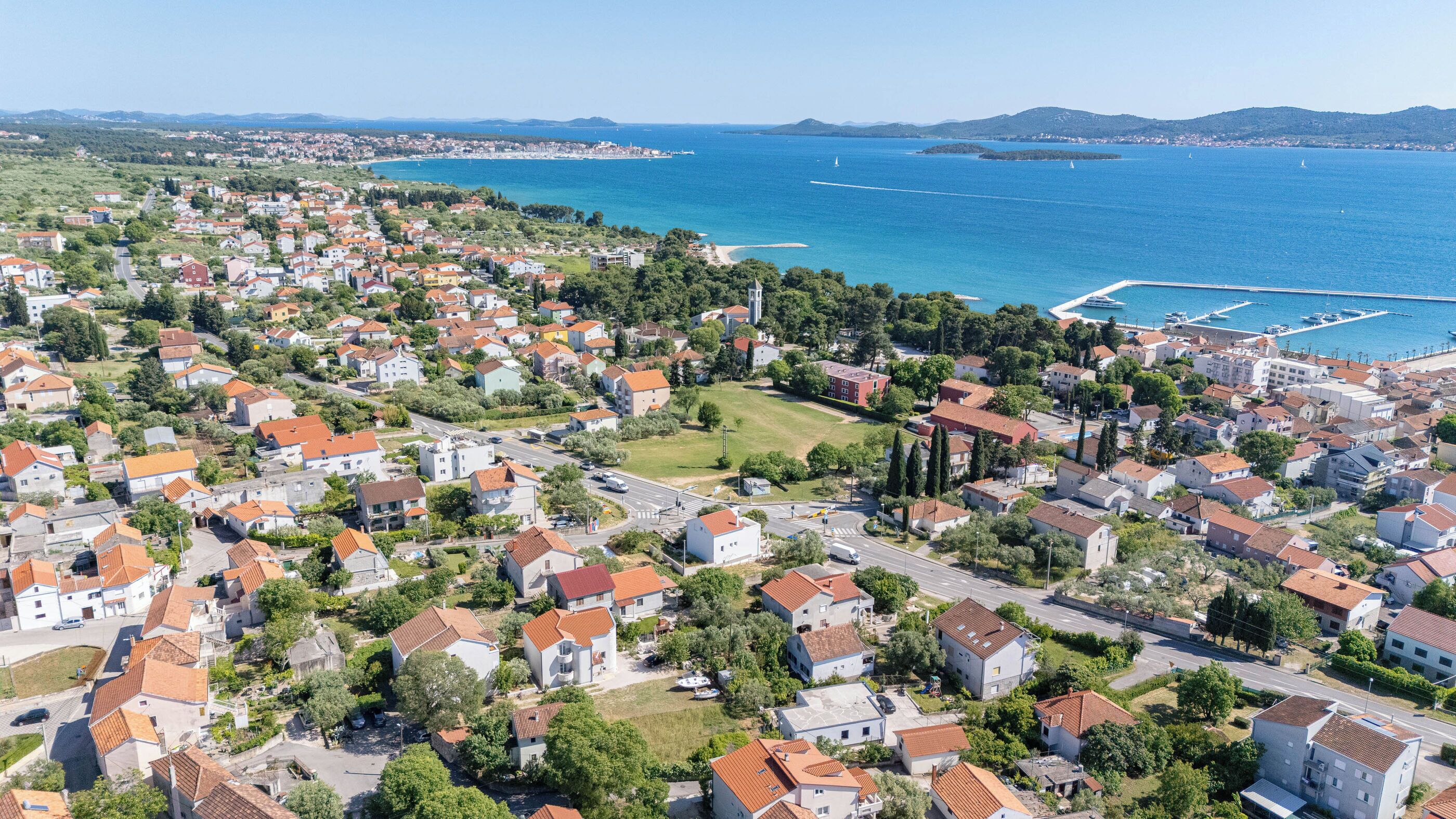 Eine Vogelperspektive einer Küstenstadt mit Wohnhäusern, einem Yachthafen und freiem Blick auf das Meer.