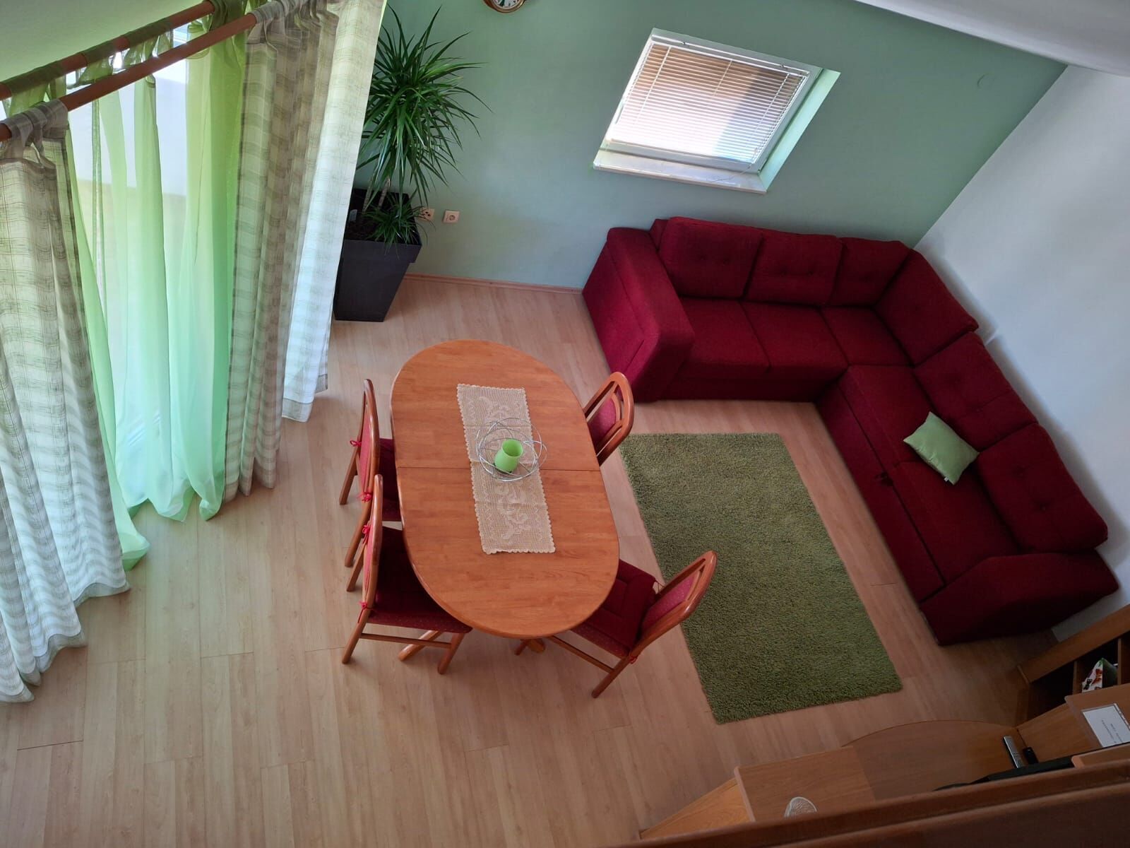 Uma sala de estar com um sofá vermelho, uma mesa de jantar com cadeiras, uma planta verde e uma janela com persianas.