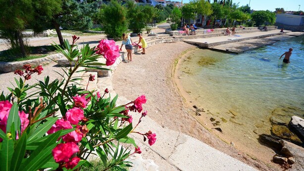A beach with clear water, people swimming, and a stone pathway. - Apartments Akustik (Sveti Filip i Jakov)