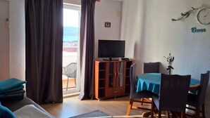 A cozy living room with a sofa, a dining table with chairs, a TV, and a view of the outdoors. - Apartments Akustik (Sveti Filip i Jakov)