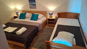 A hotel room with two beds, a nightstand with a lamp, a small shelf, and a framed picture on the wall. - Apartments Akustik (Sveti Filip i Jakov)