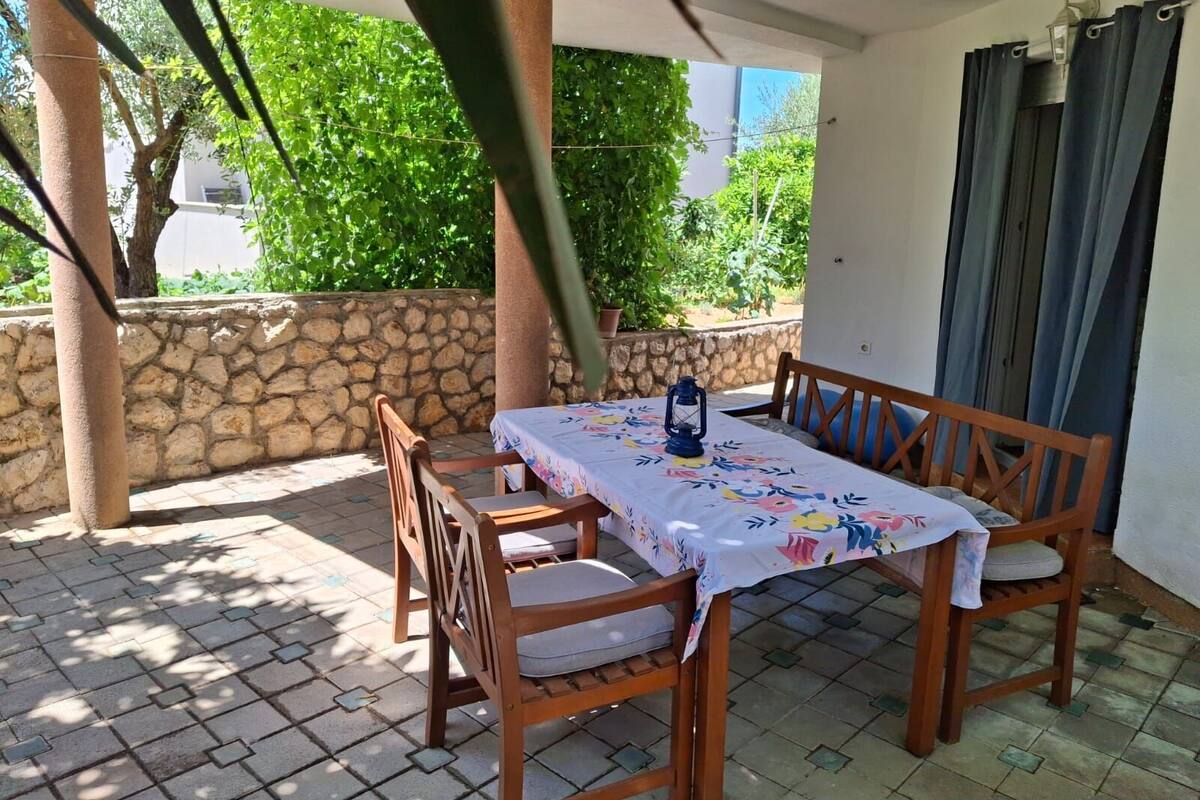 Eine Terrasse im Freien mit einem Holztisch und -stühlen, bedeckt mit einer weißen Tischdecke mit floralem Muster.