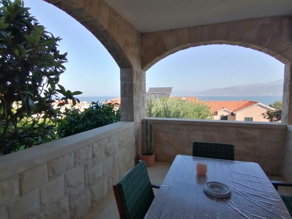 A balcony with a table and chairs, a potted plant, and a view of the sea and buildings. - Apartments Family (Postira)