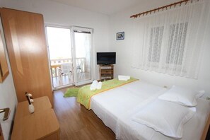 A hotel room with a bed, a television, a desk, and a sliding glass door leading to a balcony. - Apartments Family (Postira)