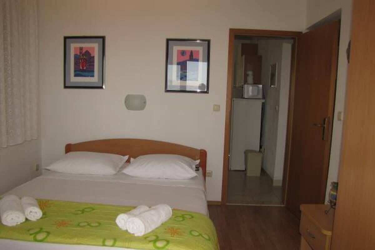 A neatly made bed with white linens and a green blanket, a wooden headboard, and two framed pictures on the wall.