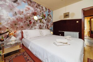 Ein Hotelzimmer mit einem großen Bett, einem Nachttisch mit Lampe, einem Heizkörper und einem Wandgemälde mit floralem Dekor.