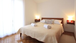 A neatly made bed with two rolled towels, a wooden headboard, and bedside lamps. - House Gianna (Sveti Filip i Jakov)