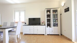 A modern kitchen with white cabinetry, a dining table with chairs, a flat-screen TV, and a cabinet with glass doors. - House Gianna (Sveti Filip i Jakov)