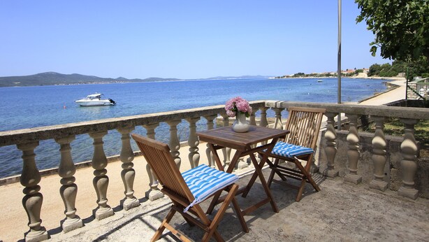 A balcony with a view of the sea, two wooden chairs with blue cushions, and a table with a vase of flowers. - House Gianna (Sveti Filip i Jakov)