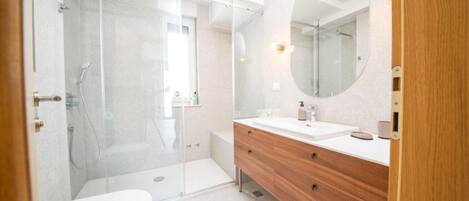 A modern bathroom with a glass shower enclosure, a white sink, and a wooden vanity.