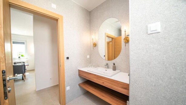 A modern bathroom with a wooden vanity, a round mirror, and a white sink. - Apartments Vrsi (Vrsi)