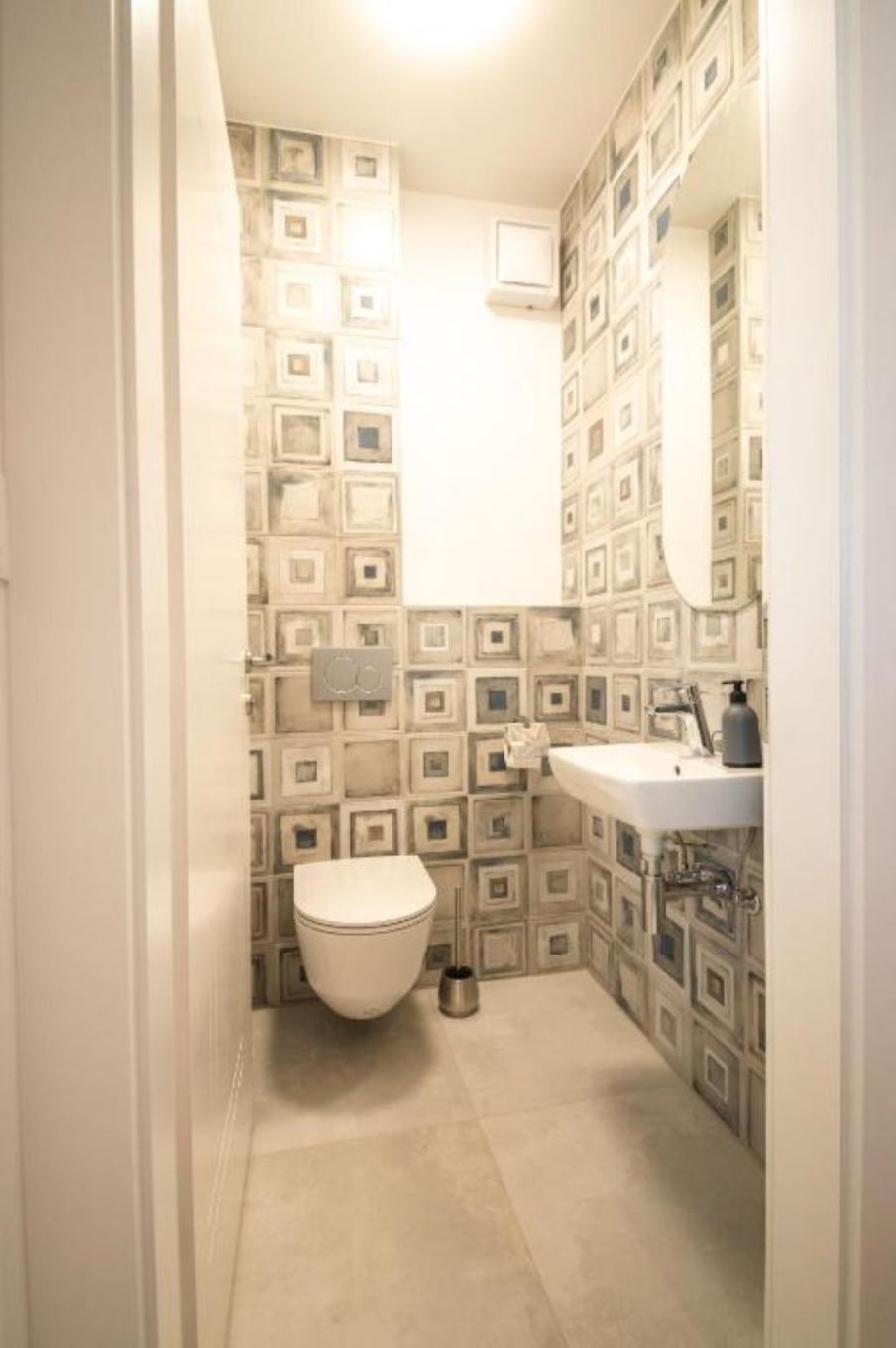 A small bathroom with a toilet, sink, and mirror. The walls have a geometric pattern.