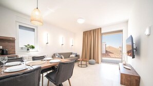 Ein moderner Essbereich mit Tisch für vier Personen, einer Couch und einem an der Wand montierten Fernseher.