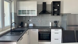 A modern kitchen with white cabinets, a black range hood, a built-in oven, and a stainless steel refrigerator. - Apartments Dobrila (Jelsa)