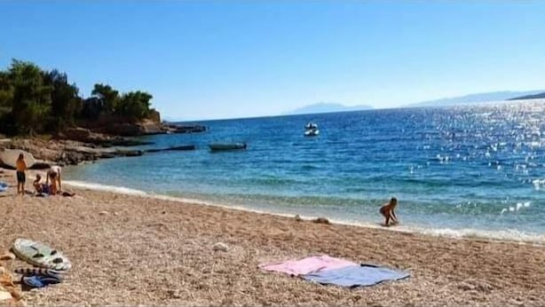 A beach with people sunbathing and swimming, clear blue water, and boats in the distance. - Apartments Dobrila (Jelsa)