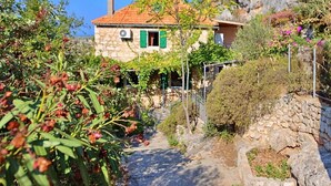 Une maison en pierre avec un toit recouvert de tuiles rouges, des volets verts et une cheminée.