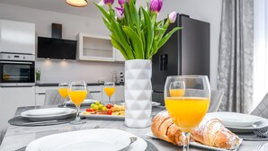Egy reggelizőasztal, rajta tányérok, narancslével teli poharak, egy croissant és egy virágos váz.