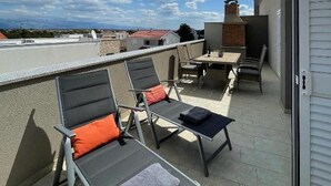 Eine Dachterrasse mit Gartenmöbeln, einem Tisch und Blick auf den Himmel und die Gebäude.
