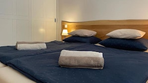 Ein ordentlich bezogenes Bett mit einem Holz-Kopfteil, einer Nachttischlampe und einer geschlossenen Tür in einem Hotelzimmer.