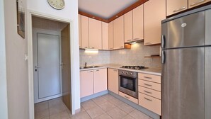A kitchen with light-colored cabinets, a stainless steel refrigerator, a stove, and a clock on the wall. - Apartment Milan (Trogir)