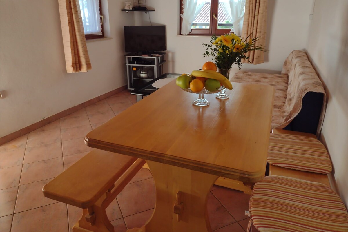 A cozy living room with a wooden dining table, a bench, a sofa, and a TV.
