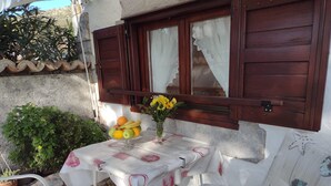 Un piccolo tavolo all'aperto con una tovaglia bianca, una ciotola di frutta e un vaso con fiori gialli.