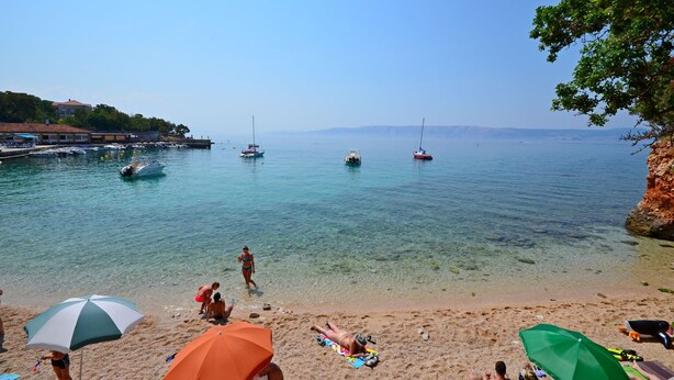 Una spiaggia con acque cristalline, barche e persone che si rilassano sotto gli ombrelloni.