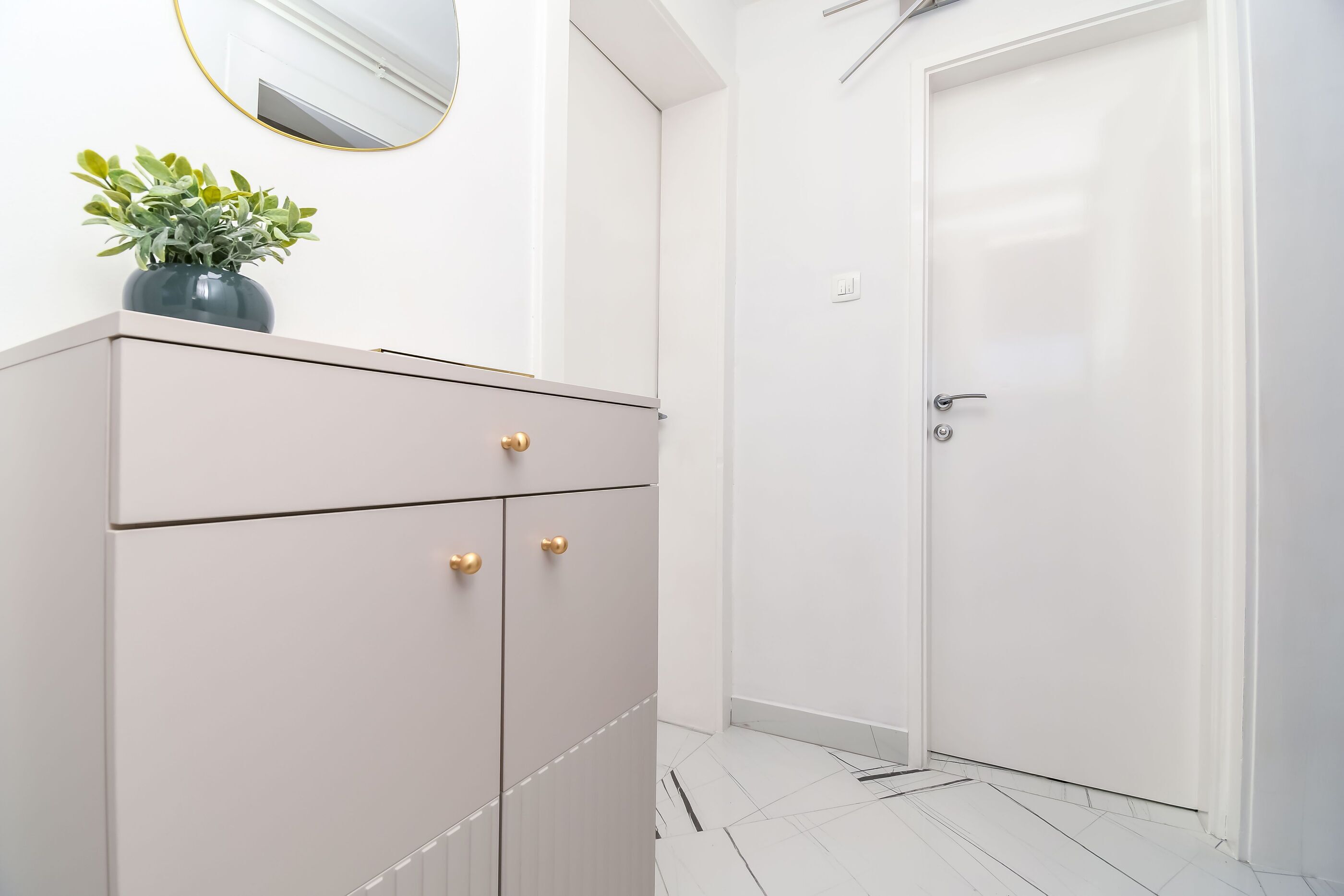 Een strakke badkamer met een wit kastje, een potplant en een deur.