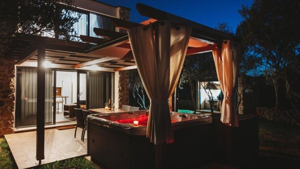 Un área moderna para jacuzzi al aire libre con cerramiento de vidrio, un patio con asientos y un muro de piedra.