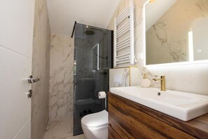 A bathroom with a marble wall, a wooden vanity, a white sink, and a glass shower enclosure.