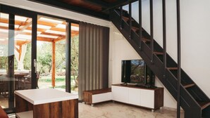 Una sala de estar moderna con un televisor sobre un mueble de madera, una escalera y un ventanal que da a un espacio exterior.