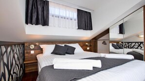 Un dormitorio moderno con una cama grande, cabecera de madera, ventana con cortinas y un espejo que refleja la habitación.
