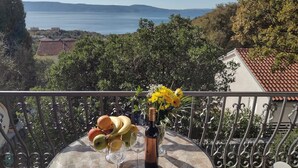 A balcony with a table set for a meal, featuring fruits and a bottle of wine, overlooking a scenic view of a lake and distant hills. - Apartment Anchi (Novi Vinodolski)