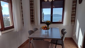 A dining area with a table set for six, a view of the sea through a window, and a vase of flowers on the table. - Apartment Anchi (Novi Vinodolski)