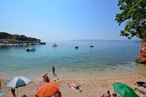 Ein Strand mit klarem Wasser, Booten und Menschen, die unter Sonnenschirmen entspannen.