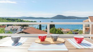 A balcony with a view of a lake and mountains, featuring two tables with striped mats and polka-dotted bowls. - Apartments Angel (Vodice)
