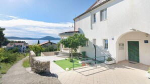 A white building with a green door, a stone wall, and a small garden. - Apartments Angel (Vodice)