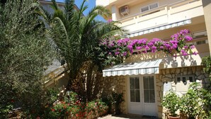 Um edifício com fachada de pedra, uma pequena entrada com porta e uma varanda com flores roxas.