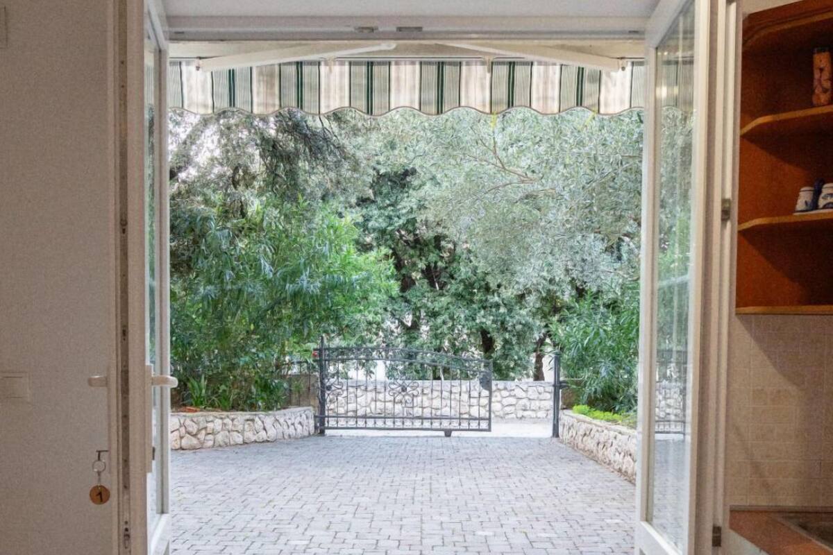 An open door leading to a paved outdoor area with a stone wall and greenery.