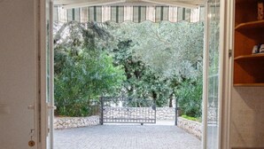 Uma porta aberta dá acesso a uma área externa pavimentada, com muro de pedra e vegetação.