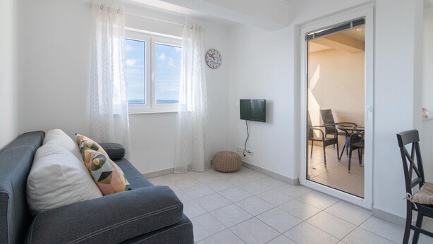 Uma sala de estar moderna com um sofá cinzento, uma televisão de tela plana e uma área de jantar com cadeiras e uma mesa.