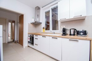 A modern kitchen with white cabinets, a stainless steel range hood, a built-in oven, a coffee maker, and a kettle on the countertop. - Apartments Apartmani Oh La La (Supetar)
