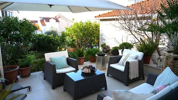 An outdoor patio area with wicker furniture, potted plants, and a large umbrella providing shade.