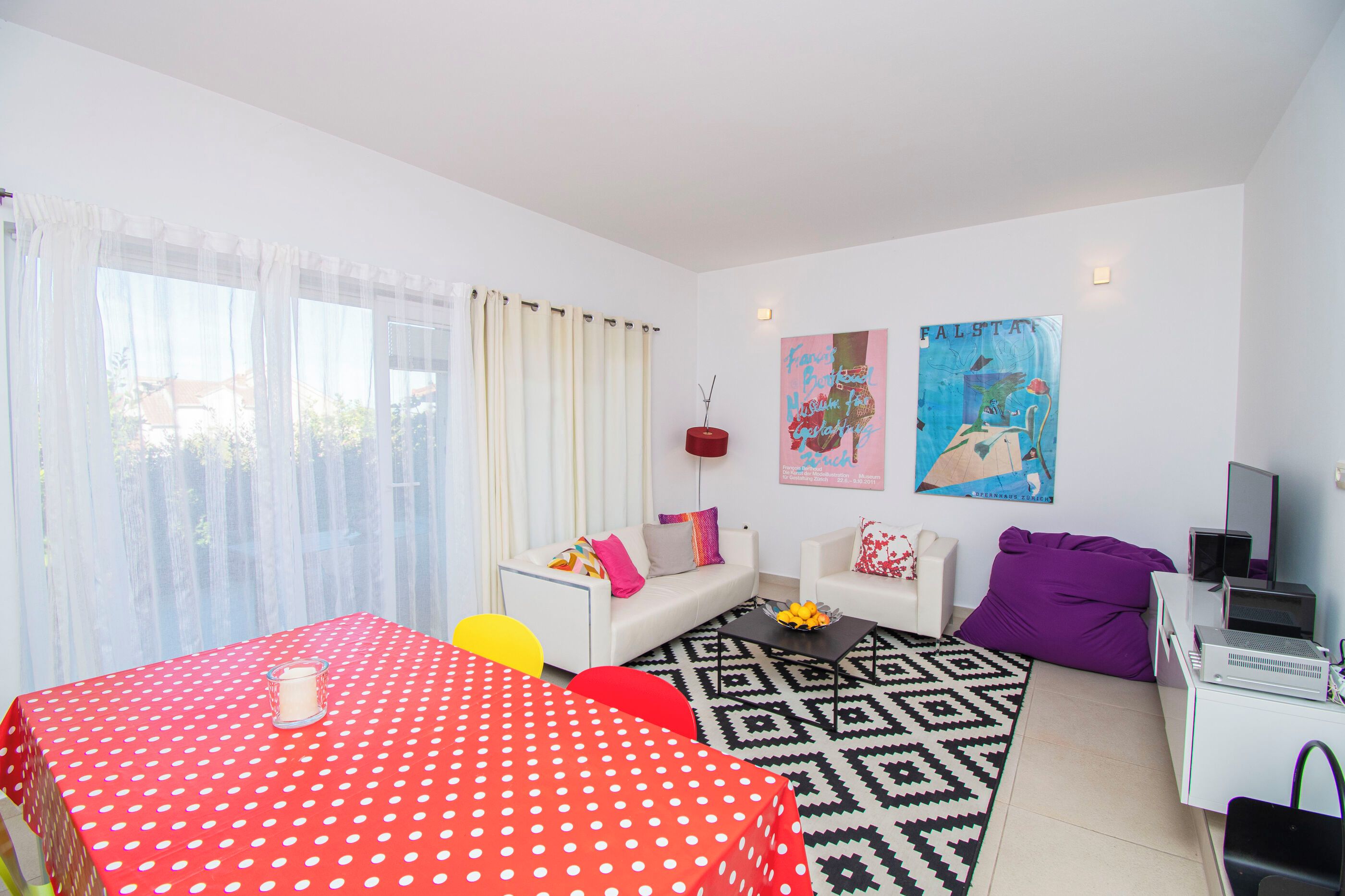A modern living room with a red polka dot table, a white sofa, a black and white patterned rug, and a painting on the wall.